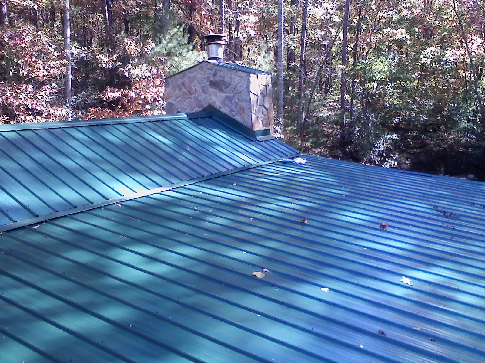 New green metal roof and stone chimney surrounded by autumn woods in Canton